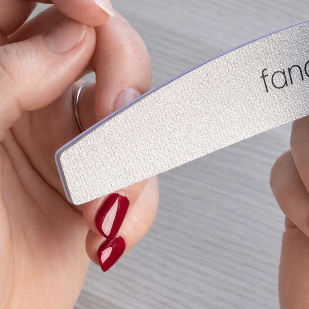 Nagel wird mit einer Nagelfeile nachgefeilt, roter Dipping Powder ist noch auf anderen Nägeln sichtbar