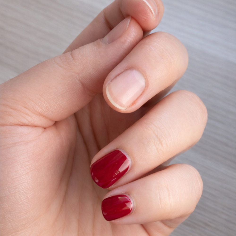 Hand mit teils lackfreien Naturnägeln und teils roten Dipping-Powder-Nägeln während des Entfernungsprozesses