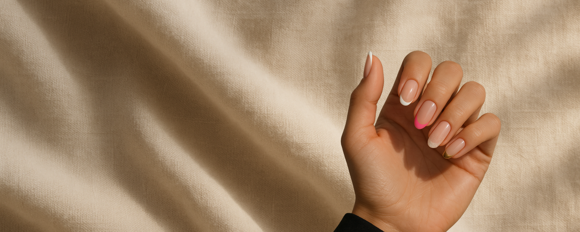 Editorial-Aufnahme einer Hand mit unterschiedlichen French Manicure Nägeln vor beige Stoffhintergrund, Variation von klassisch bis bunt.