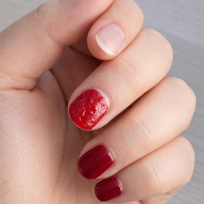 Hand mit teilweise gelöstem rotem Dipping Powder auf einem Fingernagel während der Remover-Anwendung