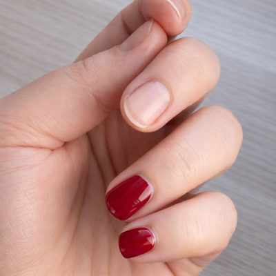 Hand mit teils lackfreien Naturnägeln und teils roten Dipping-Powder-Nägeln während des Entfernungsprozesses