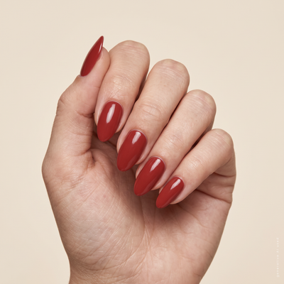 Mandel­förmige Nägel in klassischem Rot ohne Glitzer mit fancyhands® Letizia, auf beigem Stoff präsentiert.